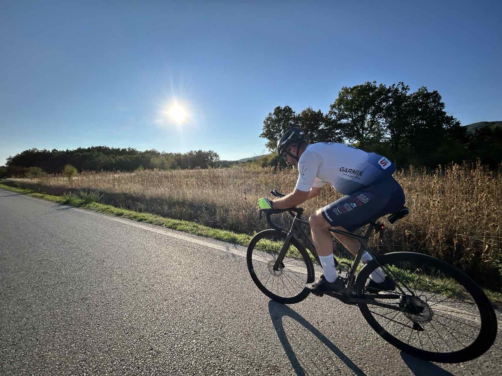 Biciklista u Garmin dresu vozi drumski bicikl osunčanim putem.
